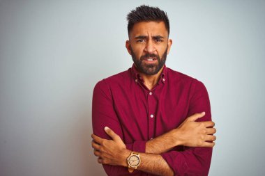 Genç Hintli adam, kırmızı şık bir gömlek giyiyor. Gri arka planda duruyor. Kış soğuğu yüzünden titriyor ve donuyor.