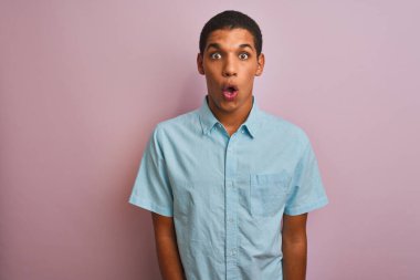 Mavi tişörtlü genç yakışıklı Arap adam pembe arka planda dikiliyor korku, korku ve heyecan dolu yüz ifadesinden korkuyor ve şok oluyor..