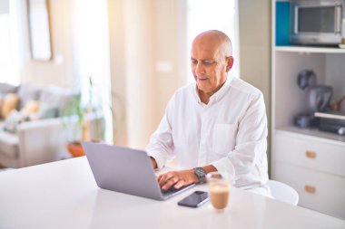 Kıdemli yakışıklı adam mutlu ve kendinden emin gülümsüyor. Evde dizüstü bilgisayar kullanıp kahve içmek.