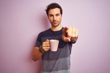 Dövmeli genç yakışıklı adam izole edilmiş pembe arka planda kahve içerek kamerayı işaret ediyor ve sen, el işareti, ön taraftan pozitif ve kendinden emin bir jest.