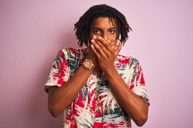 Tatilde saçı rastalı bir Afro adam çiçekli bir gömlek giyiyor pembe arka planda, ağzı yanlışlıkla ellerle örterek şok ediyor. Gizli konsept.