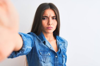 Kot gömlek giyen güzel bir kadın, izole edilmiş beyaz arka plan şüphecisi ve gergin bir şekilde kamerayla selfie çekiyor, sorun yüzünden kaşlarını çatıyor. Negatif kişi.