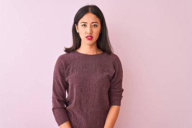 Mor süveter giyen genç Çinli kadın pembe arka planda duruyor ve yüzünde ciddi bir ifade var. Basit ve doğal bir şekilde kameraya bakıyorsun..