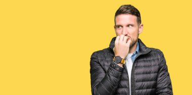 Kışlık palto giyen yakışıklı adam stresli ve gergin görünüyor elleri ağızda tırnak ları ısırıyor. Anksiyete sorunu.