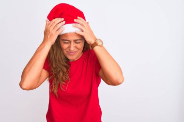 Orta yaşlı olgun bir kadın, izole bir arka plan üzerine noel şapkası takıp acı ve migren yüzünden çaresiz ve stresli bir şekilde acı çekiyor. Ellerini başının üstüne koy..