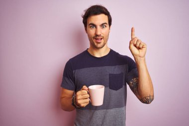 Dövmeli genç yakışıklı adam izole edilmiş pembe arka planda kahve içerken bir fikir ya da soru işareti ile şaşırdı.