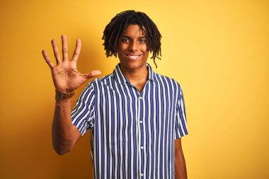 Rastgele çizgili tişörtler giyen Afro adam izole edilmiş sarı arka planda beş numarayı gösterirken kendinden emin ve mutlu bir şekilde gülümsüyor..