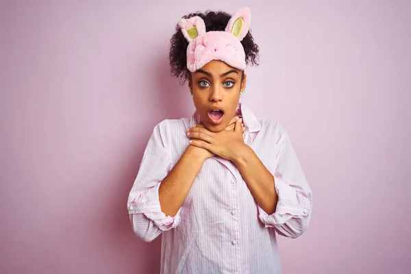 アフリカ系アメリカ人の若い女性がパジャマを着て ピンクの背景にマスクをして息を吹きかけている 健康上の問題窒息と自殺の概念 — ストック写真