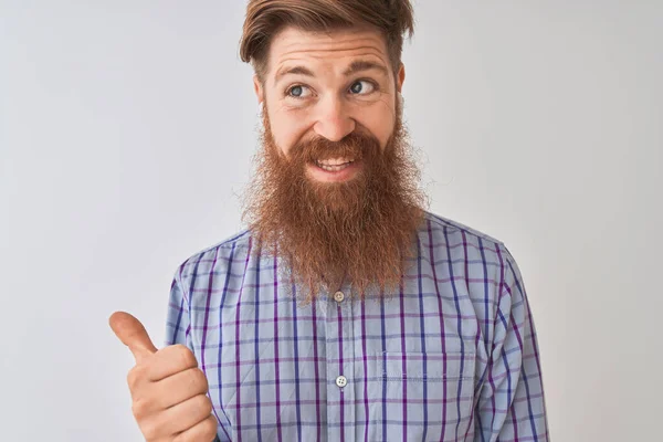 Redhead irish man listening to music using wireless earphones over isolated white background smiling with happy face looking and pointing to the side with thumb up.
