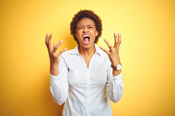 African american business woman over isolated yellow background crazy and mad shouting and yelling with aggressive expression and arms raised. Frustration concept.
