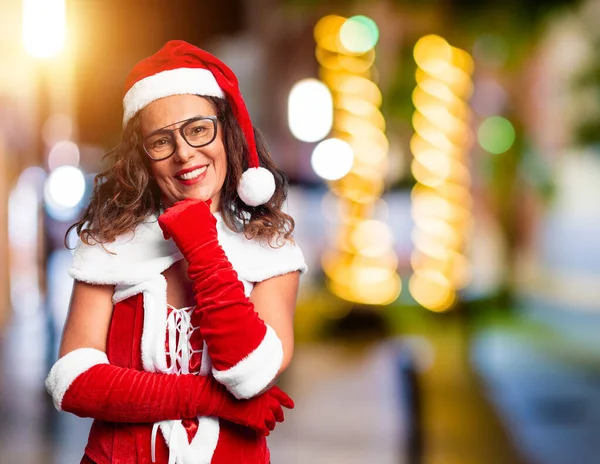 中年妇女穿着圣诞老人的服装 面带微笑地看着相机 双臂交叉 双手托着下巴 看起来很自信 积极地思考 — 图库照片