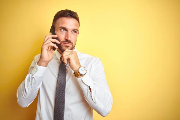 黄色の隔離された背景深刻な顔の上に電話で話している若いハンサムなビジネスマンの質問について考えて 非常に混乱したアイデア — ストック写真