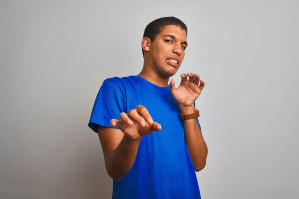 Young handsome arab man wearing blue t-shirt standing over isolated white background disgusted expression, displeased and fearful doing disgust face because aversion reaction. With hands raised. Annoying concept.