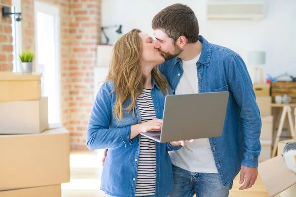 Young couple using computer laptop standing on a room around cardboard boxes, happy for moving to a new apartment