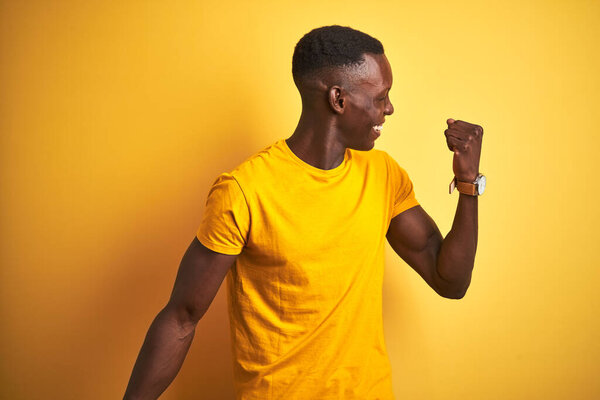 Young african american man wearing casual t-shirt standing over isolated yellow background Dancing happy and cheerful, smiling moving casual and confident listening to music