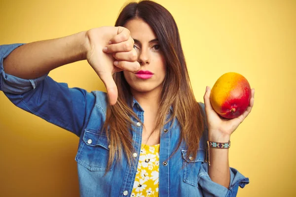 Young Beautiful Woman Eating Fresh Healthy Mango Yellow Background Angry — Stock Photo, Image