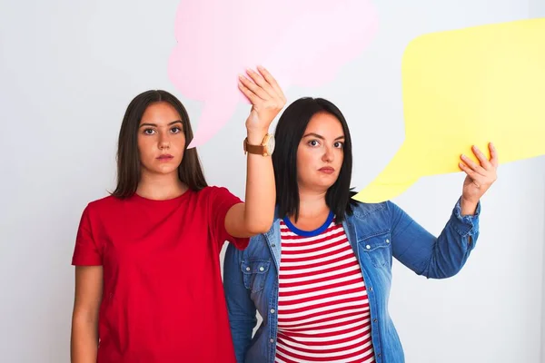 Young beautiful women holding speech bubble standing over isolated white background with a confident expression on smart face thinking serious