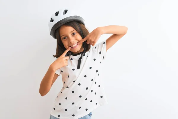 漂亮的小女孩戴着安全的自行车头盔 站在孤独的白色背景上 开心地微笑着 用手指 牙齿和嘴指指指点点 牙齿健康概念 — 图库照片