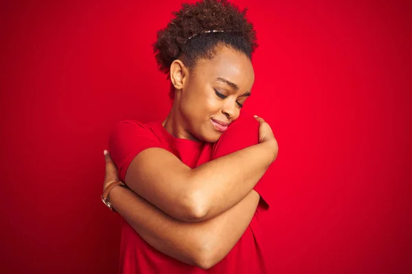 Young beautiful african american woman with afro hair over isolated red background Hugging oneself happy and positive, smiling confident. Self love and self care