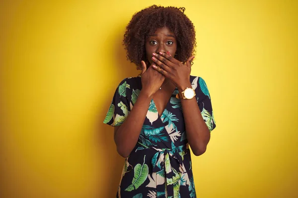 孤立した黄色の背景の上に夏の花のドレスを着て若いアフリカのアフロ女性は間違いのために手で口をカバーショックを受けた 秘密概念 — ストック写真