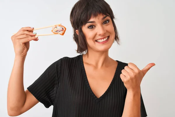 孤立した白い背景の上に箸で寿司を食べ 幸せな顔を笑顔で親指で横に示す若い美しい女性 — ストック写真