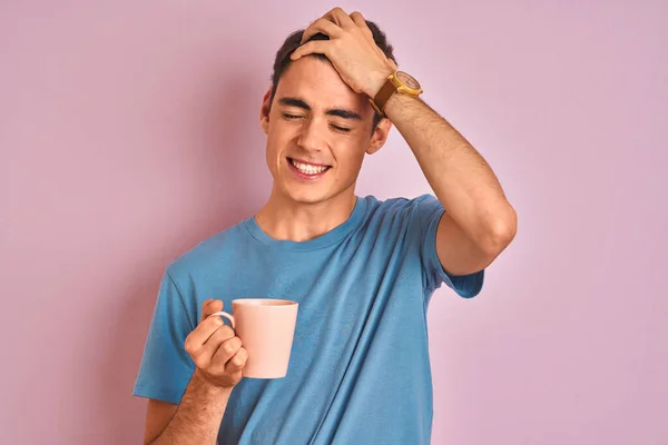 Teenager boy drinking a cup of coffee over isolated pink background stressed with hand on head, shocked with shame and surprise face, angry and frustrated. Fear and upset for mistake.