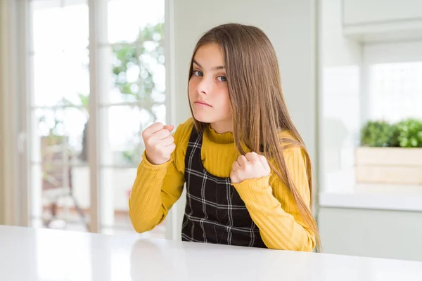 Young beautiful blonde kid girl wearing casual yellow sweater at home Ready to fight with fist defense gesture, angry and upset face, afraid of problem
