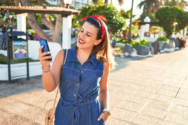 夏の晴れた日に街を歩いて幸せな笑顔の若い美しい女性スマートフォンを使用して — ストック写真