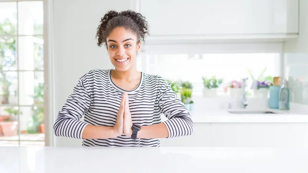 Beautiful african american woman with afro hair wearing casual striped sweater praying with hands together asking for forgiveness smiling confident.