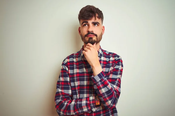 Young man wearing casual shirt standing over isolated white background with hand on chin thinking about question, pensive expression. Smiling with thoughtful face. Doubt concept.