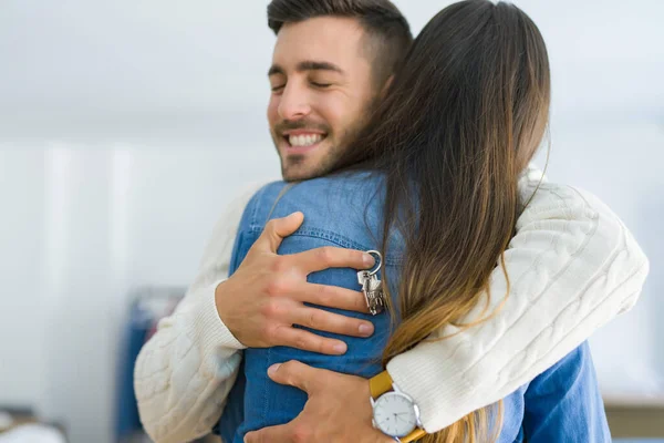 Casal jovem se mudando para uma nova casa, abraçando no amor mostrando chaves — Fotografia de Stock