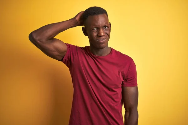 Young african american man wearing red t-shirt standing over isolated yellow background confuse and wonder about question. Uncertain with doubt, thinking with hand on head. Pensive concept.