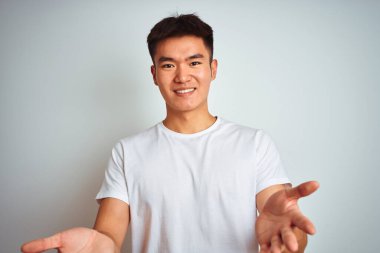 Asyalı genç bir Çinli tişört giyiyor. İzole edilmiş beyaz arka planda duruyor. Gülümsüyor, yardım eli uzatıyor ve kabul ediyor..