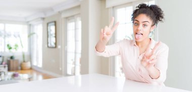 Afro saçlı, ağzı açık gülümseyen ve parmaklarını her iki elini de zafer işareti yaparken gösteren güzel Afro-Amerikan kadını geniş açılı. İki numara..