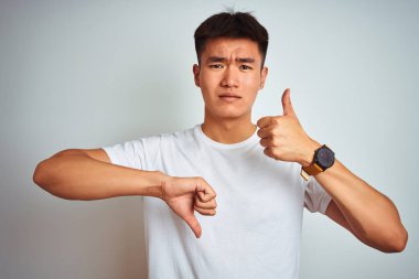 Asyalı genç bir Çinli tişört giyiyor beyaz arka planda dikiliyor. Baş parmak işareti yapıyor, anlaşmazlık ve anlaşma ifadesi takınıyor. Çılgın çatışma