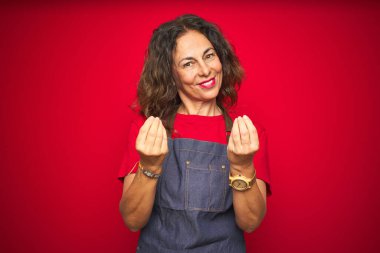 Kırmızı arka planda önlük giyen orta yaşlı bir kadın. Elleriyle para hareketi yapıyor. Maaş ödemesi istiyor.