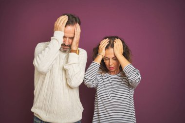 Güzel bir orta yaşlı çift, izole edilmiş mor arka plan üzerine kazak giyip acı ve migren yüzünden çaresiz ve stresli bir baş ağrısı çekiyor. Ellerini başının üstüne koy..