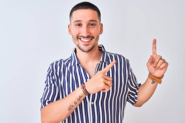 Deniz çizgili gömlek giyen genç yakışıklı arka planda duruyor gülümsüyor ve kameraya bakıyor iki eliyle ve parmaklarıyla işaret ediyor..