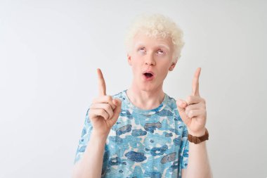 Ayrı beyaz arka plan üzerinde duran gündelik tişört giyen genç albino adam şaşırmış ve şaşırmış bir şekilde parmaklarıyla işaret ediyor ve kollarını kaldırıyordu..