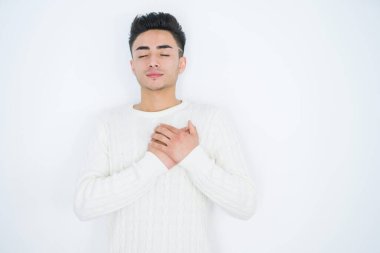 Beyaz tenli yakışıklı genç bir adam. Elleri göğsünde, gözleri kapalı gülümsüyor ve yüzünde minnet ifadesi var. Sağlık kavramı.