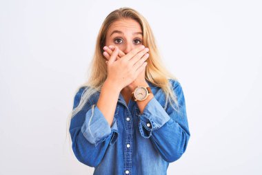 İzole edilmiş beyaz arka plan üzerinde sıradan bir kot gömlek giyen genç ve güzel bir kadın yanlışlıkla ağızlarını kapatarak şok geçirdi. Gizli konsept.
