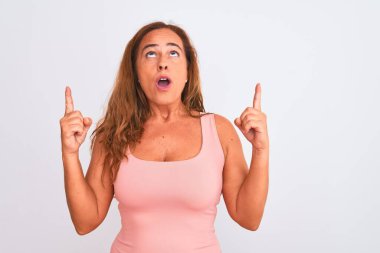 Orta yaşlı olgun bir kadın beyaz bir geçmişin başında durmuş şaşkın ve şaşırmış bir şekilde yukarı bakıyor ve parmaklarıyla işaret ediyor ve kollarını kaldırıyordu..