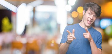 Fotoğraf makinesi ile mutlu ve komik yüz için parmakları işaret izole arka plan üzerinde mavi t-shirt giyen genç yakışıklı adam. İyi enerji ve vibes.