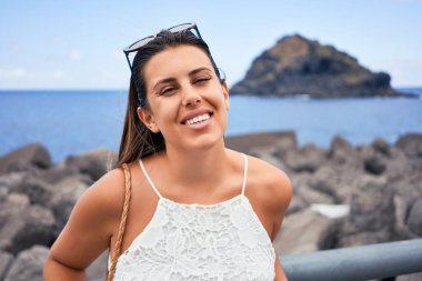 Güzel genç bir kadın kumsalda yürüyor okyanus manzarasının tadını çıkarıyor yaz tatilinde gülümsüyor.