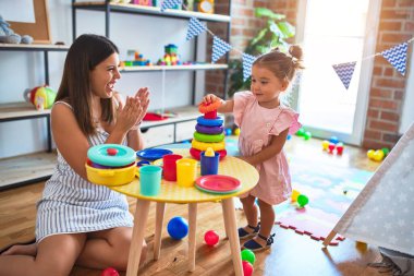 Genç, güzel öğretmen ve bebek, anaokulundaki masada halkalar kullanarak piramit inşa ediyorlar.