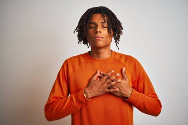 Turuncu kazaklı Afro-Amerikan bir adam izole edilmiş beyaz arka planda elleri göğsünde, gözleri kapalı ve yüzünde minnet dolu bir jest ile gülümsüyor. Sağlık kavramı.