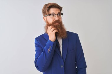 Genç kızıl İrlandalı işadamı takım elbise ve gözlük giyen izole beyaz arka plan üzerinde el çene soru, dalgın ifade düşünme. Düşünceli bir yüzle gülümsüyor. Şüphe kavramı.