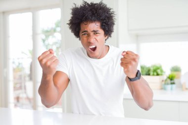 Genç Afro-Amerikalı adam, günlük beyaz tişörtler giyip kızgın ve kızgın bir şekilde evde oturmuş öfkeyle bağırırken yumruklarını kaldırıyordu. Öfke ve agresif kavram.