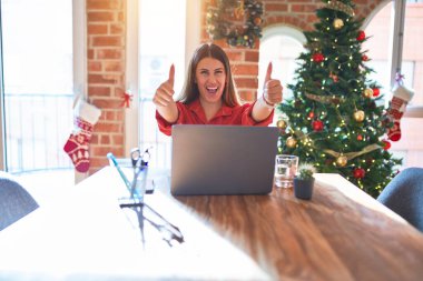 Güzel bir kadın evinde dizüstü bilgisayarla oturup Noel ağacının etrafında el hareketlerini onaylıyor, gülümseyerek ve başarıya sevinerek gülümsüyor. Kazanan jest.