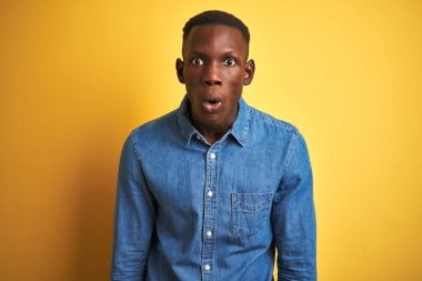 Kot gömlek giyen genç Afro-Amerikalı adam izole edilmiş sarı arka planda duruyor. Şaşırtıcı bir ifade, korku ve heyecan dolu bir yüz ifadesi var..